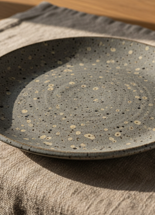 Single speckled grey stoneware plate on rustic linen table setting